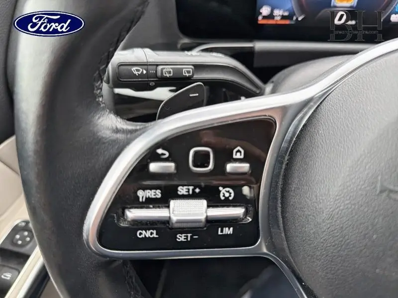Gros plan sur les commandes au volant cuir noir de la Mercedes Classe B 250 e, avec palettes et boutons multifonctions.