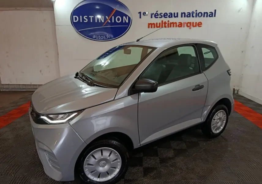 Aixam Ambition 0.5 City Pack gris clair en 3/4 avant droit, avec rétroviseur caméra côté conducteur visible.