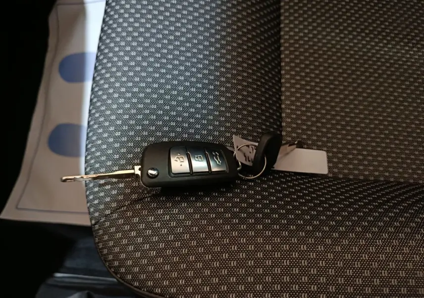 Clé de voiture AIXAM AMBITION 0.5 CITY PACK posée sur un siège tissu gris à motifs, vue rapprochée intérieure.