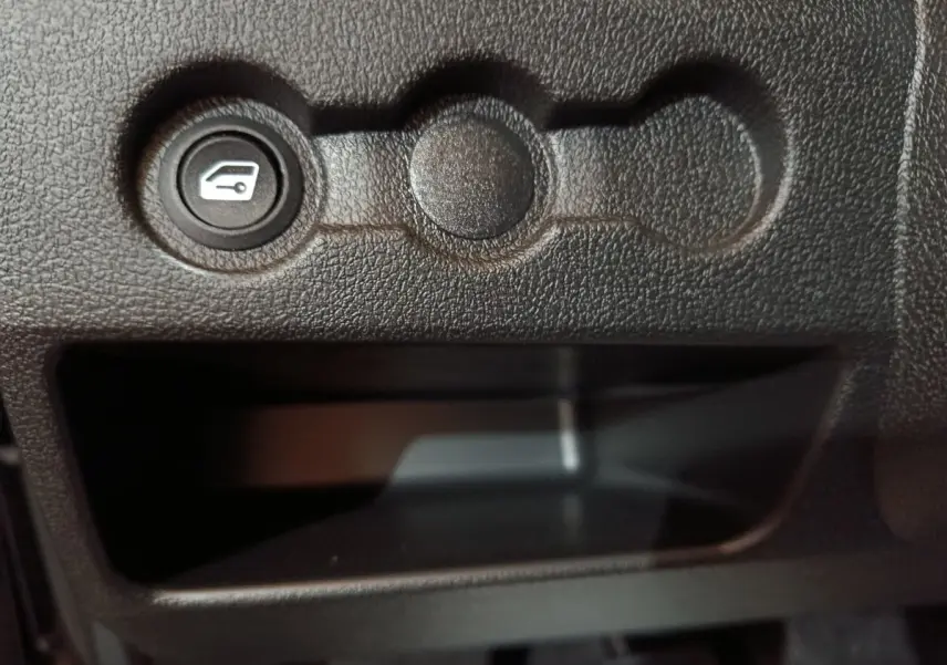 Bouton de commande de coffre sur tableau de bord noir texturé d'une Aixam Ambition 0.5 City Pack 2026.