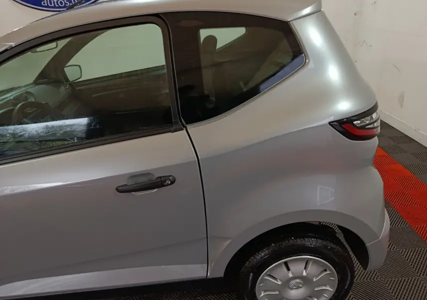 Vue latérale côté droit d'une Aixam Ambition 0.5 City Pack gris clair, mettant en valeur la porte arrière et le feu arrière.