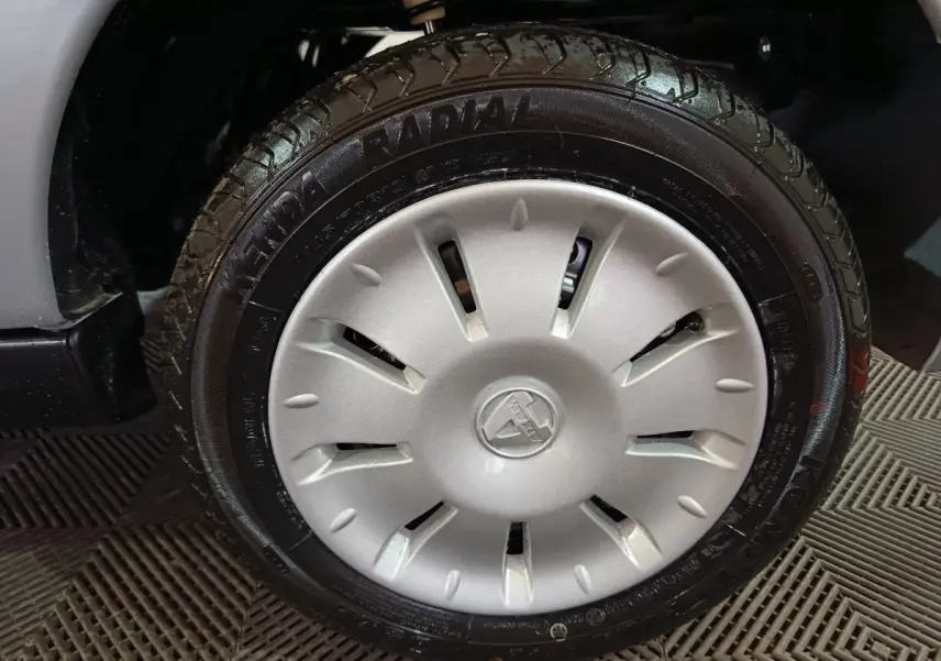 Gros plan sur la roue avant gauche d'une Aixam Ambition gris clair avec jante et logo central visibles.