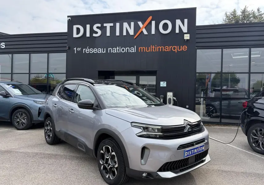 Vue 3/4 avant droit d’un Citroën C5 Aircross gris métal avec toit noir et jantes alliage bi-ton devant un concessionnaire.