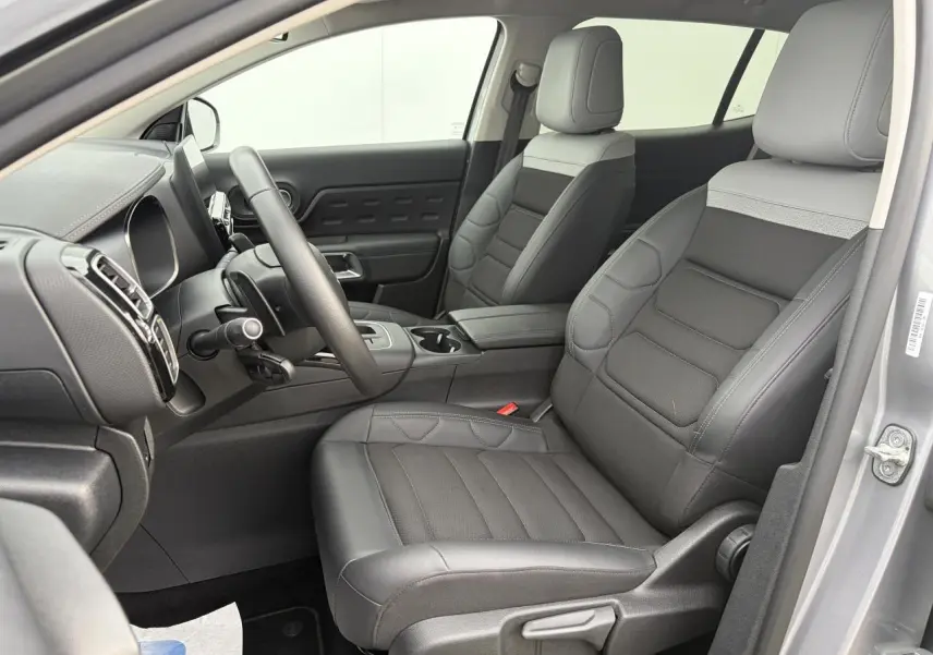 Vue intérieure côté conducteur du Citroën C5 Aircross 2024 gris métal, sièges bi-ton gris avec volant cuir et console centrale.
