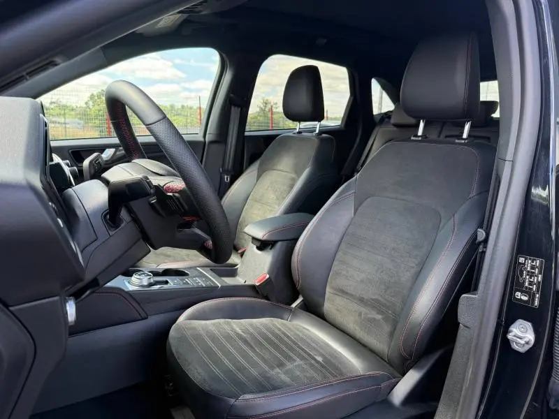 Vue intérieure côté conducteur du Ford Kuga noir Agate 2023, sièges sport en tissu et cuir avec surpiqûres rouges.