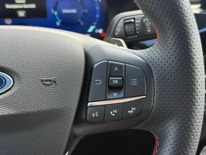 Gros plan sur les commandes multifonctions à droite du volant cuir perforé avec surpiqûres rouges du Ford Kuga noir Agate 2023.