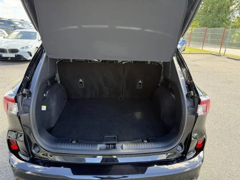 Vue arrière du coffre ouvert du Ford Kuga noir Agate Métallisée, montrant un espace de chargement propre et spacieux.