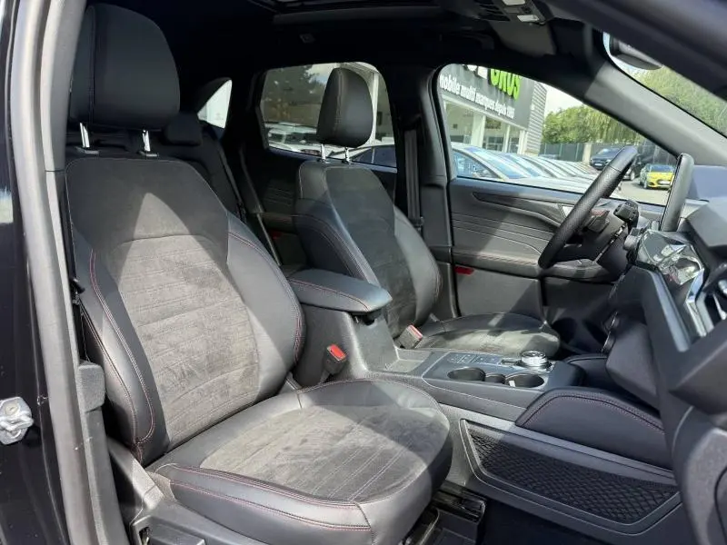 Vue intérieure avant du Ford Kuga 2023 noir Agate, sièges sport en tissu et simili cuir avec surpiqûres rouges.