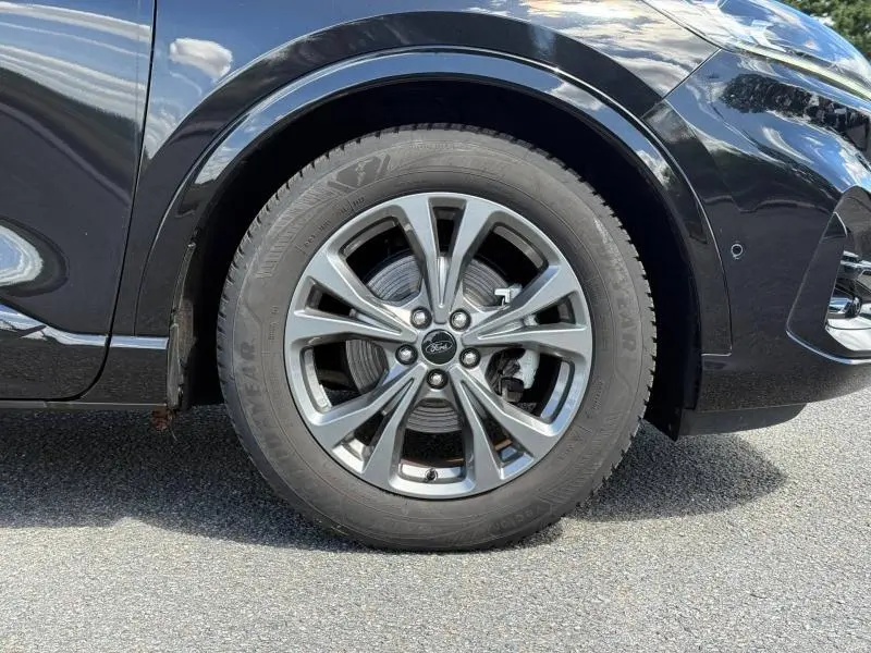 Gros plan sur la roue avant droite du Ford Kuga noir Agate Métallisée, avec jante alliage et logo Ford au centre.