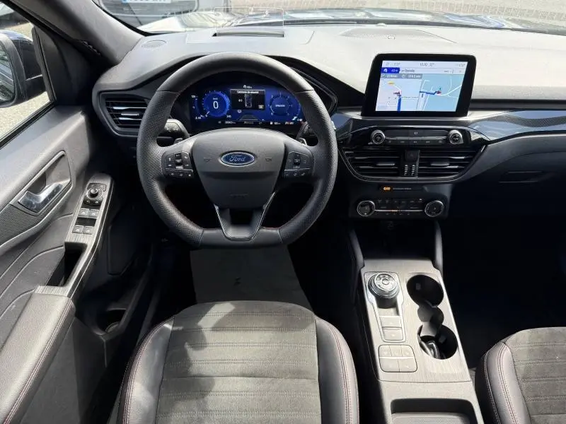 Vue intérieure avant du Ford Kuga 2023 noir Agate, volant cuir multifonction et écran tactile GPS lumineux.
