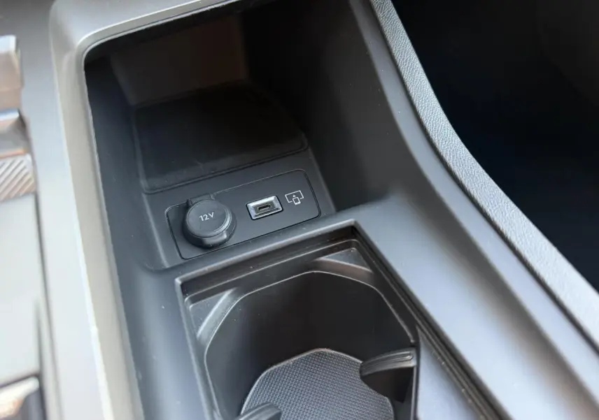 Gros plan sur la console centrale noire de la Peugeot 308 2025, montrant prise 12V et port USB.