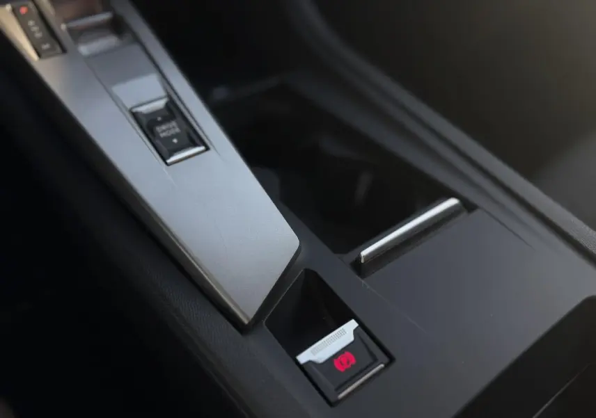 Gros plan sur la console centrale noire de la Peugeot 308 2025, mettant en valeur le frein de parking électrique.