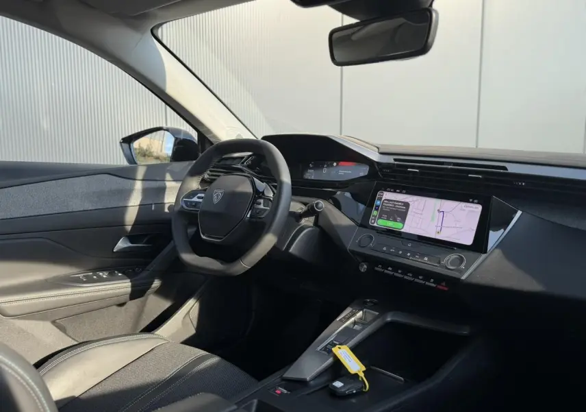 Vue intérieure côté conducteur de la Peugeot 308 2025, volant cuir, écran tactile 10 pouces avec navigation affichée.