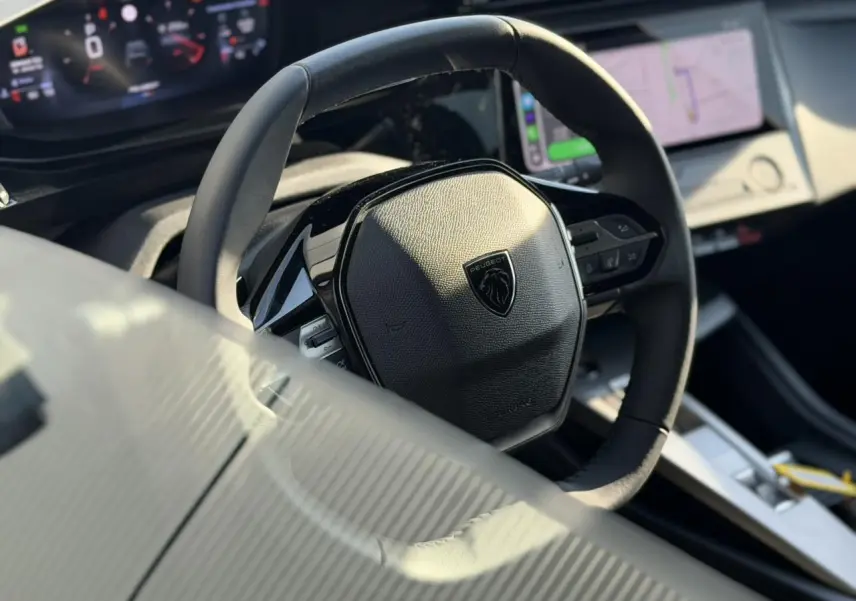 Vue rapprochée du volant cuir noir de la Peugeot 308 2025 avec tableau de bord numérique et écran tactile visible.
