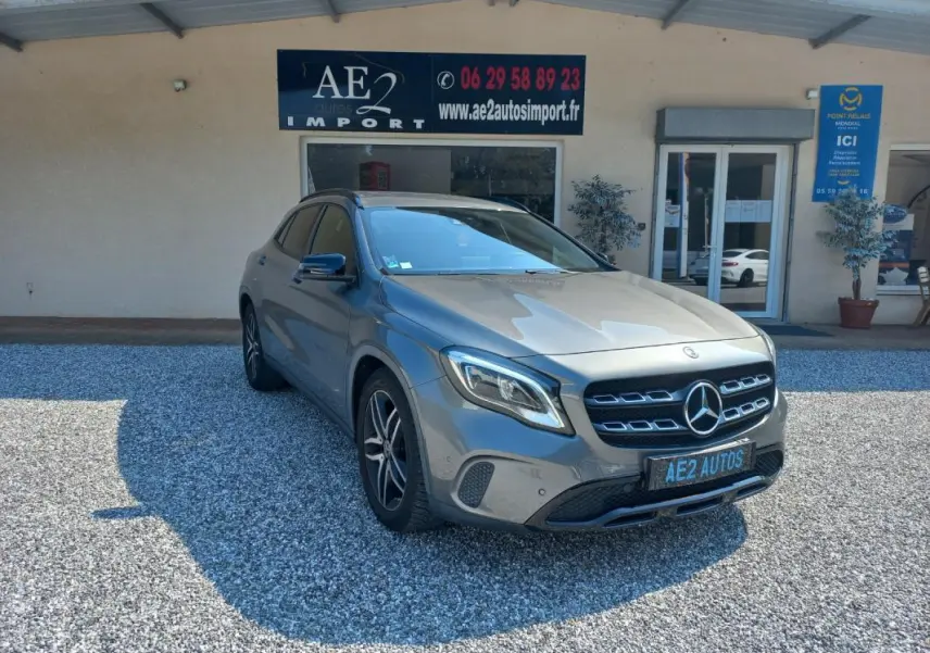 Mercedes GLA gris 3/4 avant droit, avec calandre distinctive et jantes alliage, stationné devant un bâtiment commercial.