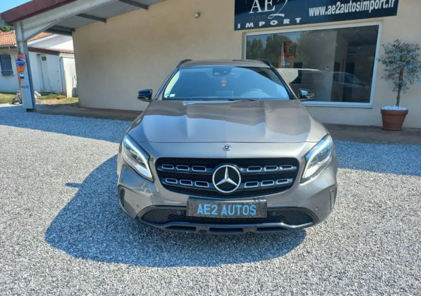 Mercedes GLA gris vue de face, mettant en valeur la calandre distinctive et les phares LED, stationné devant un bâtiment.