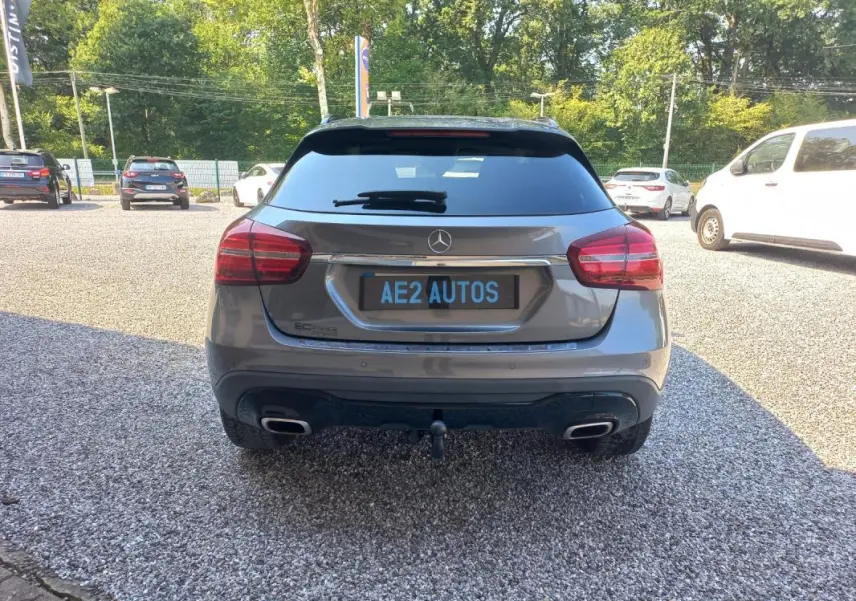 Vue arrière d'une Mercedes GLA gris 2019 avec double sortie d'échappement et attelage visible sur un parking extérieur.