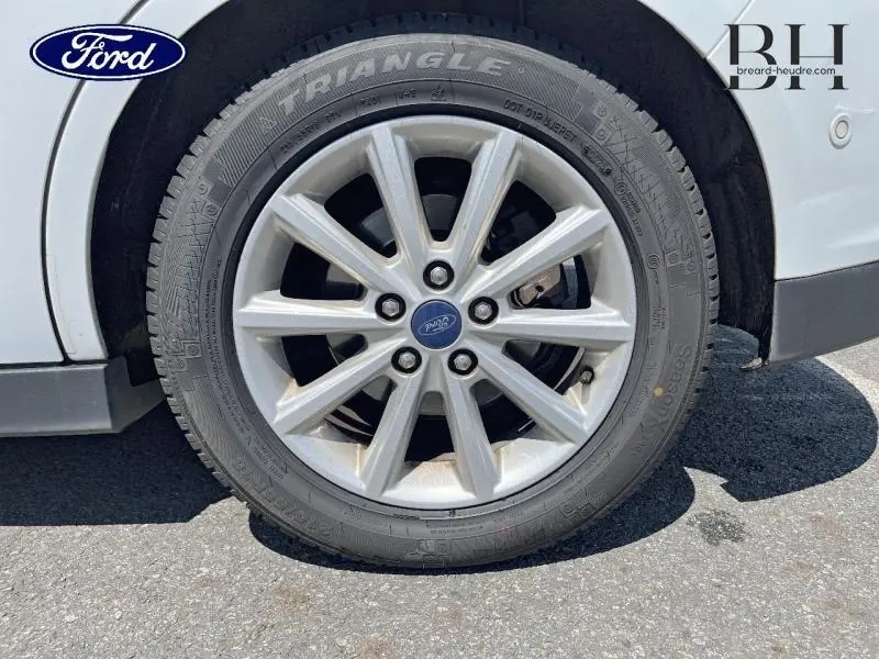 Gros plan sur la roue avant droite d'un Ford Grand C-MAX blanc Glacier avec jante alliage et logo Ford central.
