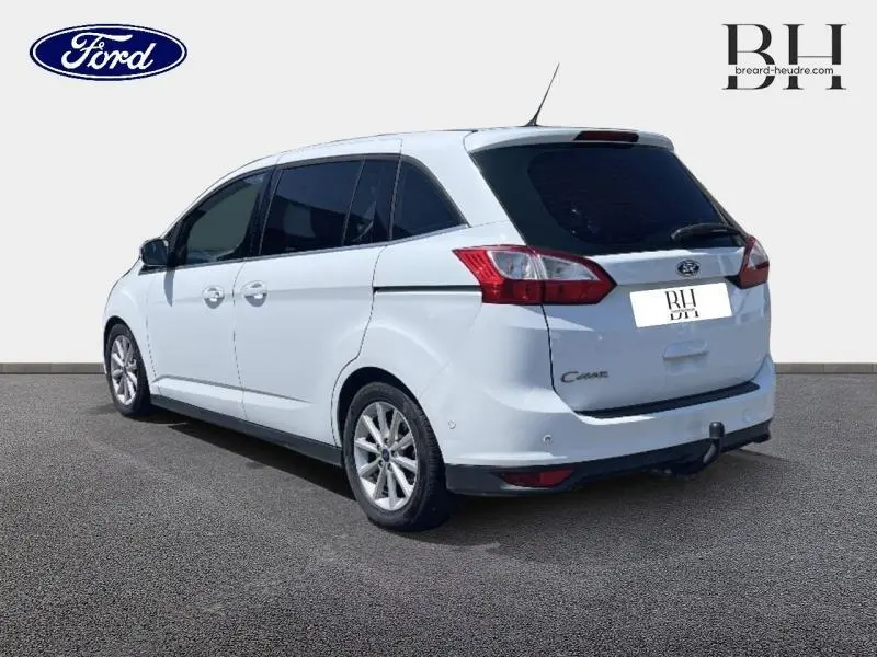 Vue 3/4 arrière droite d'un Ford Grand C-MAX blanc Glacier avec attelage et vitres arrière surteintées.