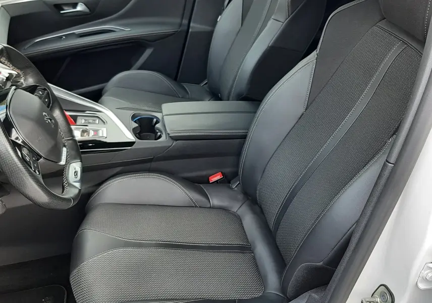 Intérieur côté conducteur du Peugeot 3008 2022, sièges noirs en cuir et tissu avec console centrale et volant visibles.