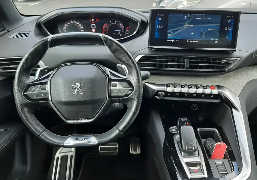 Vue intérieure frontale du poste de conduite du Peugeot 3008 blanc nacré, avec volant compact, écran tactile et console moderne.