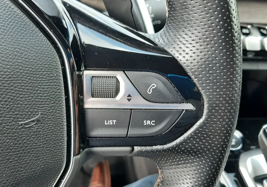 Gros plan sur les commandes gauche du volant en cuir perforé noir du Peugeot 3008 blanc nacré, avec boutons téléphone et liste.