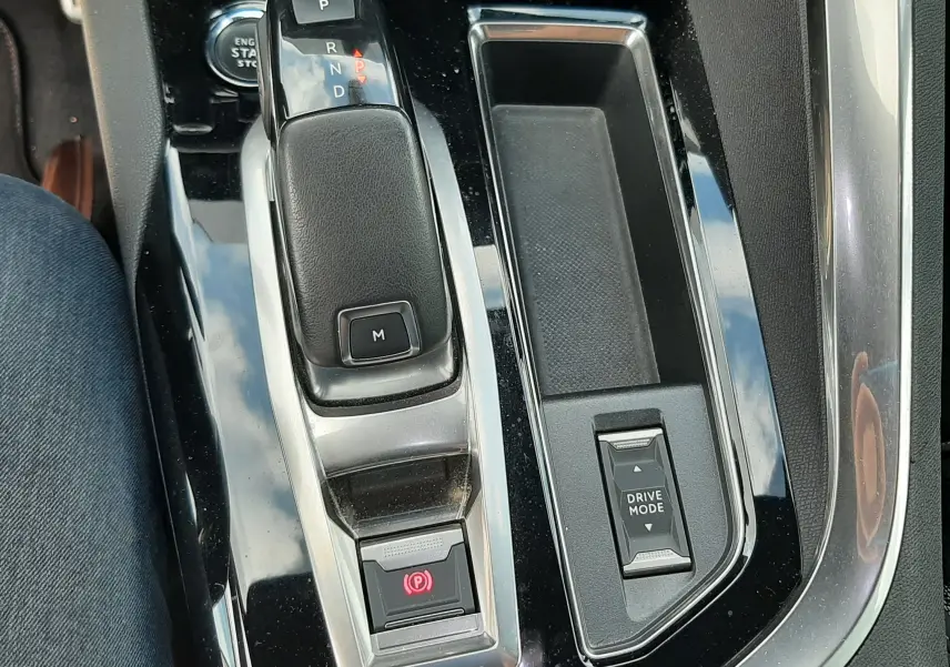 Vue rapprochée de la console centrale noire brillante du Peugeot 3008 1.5 BlueHDi, avec levier de vitesse automatique et bouton Drive Mode.
