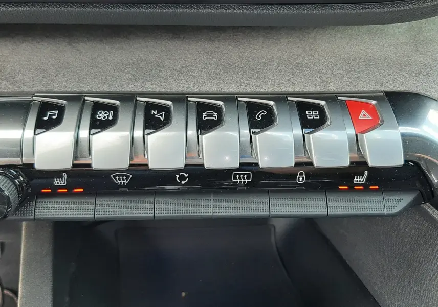 Gros plan sur la rangée de boutons argentés et noirs du tableau de bord du Peugeot 3008 blanc nacré, avec voyants rouges allumés.