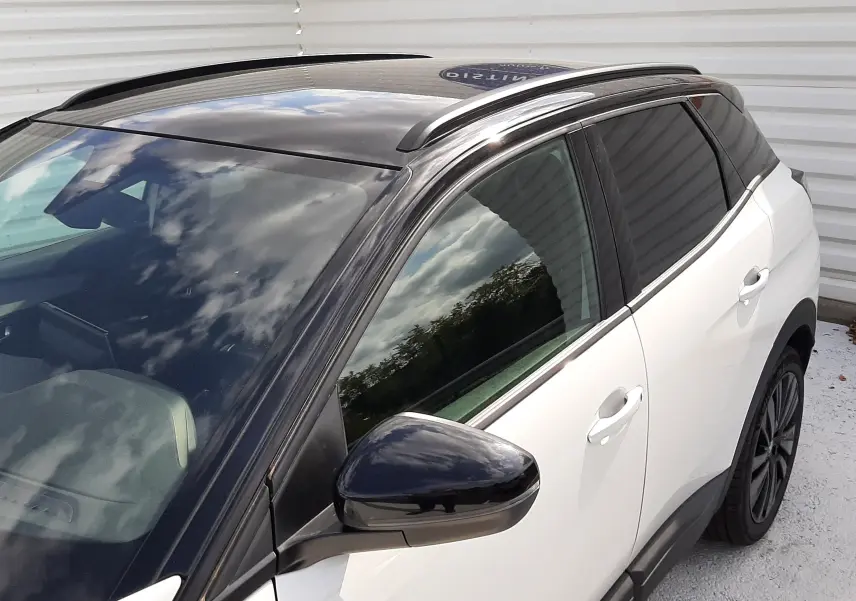 Vue 3/4 avant droit du Peugeot 3008 blanc nacré avec toit noir brillant et rétroviseur assorti, badge GT visible.