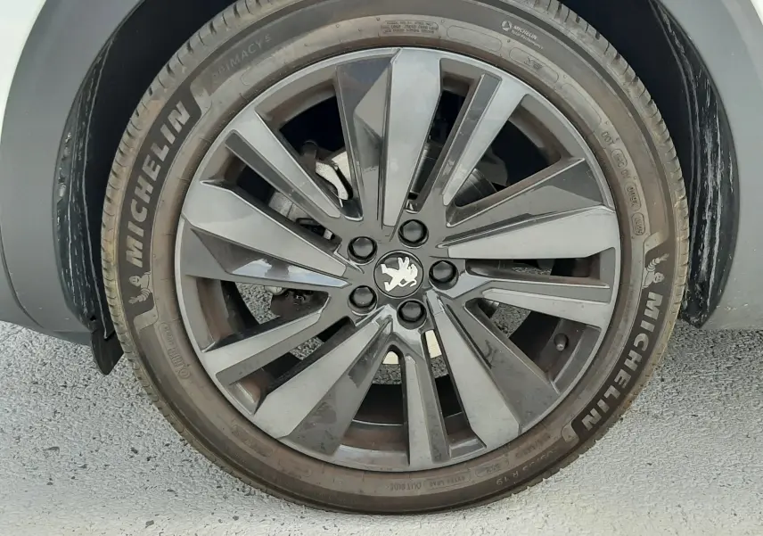 Gros plan sur la roue avant droite du Peugeot 3008 blanc nacré avec jante alliage gris foncé et logo lion central.
