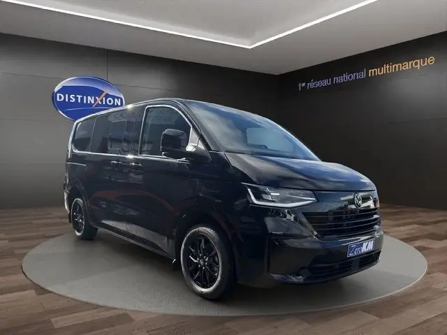Volkswagen Transporter noir en vue 3/4 avant droit, avec jantes noires et phares LED dans un showroom.