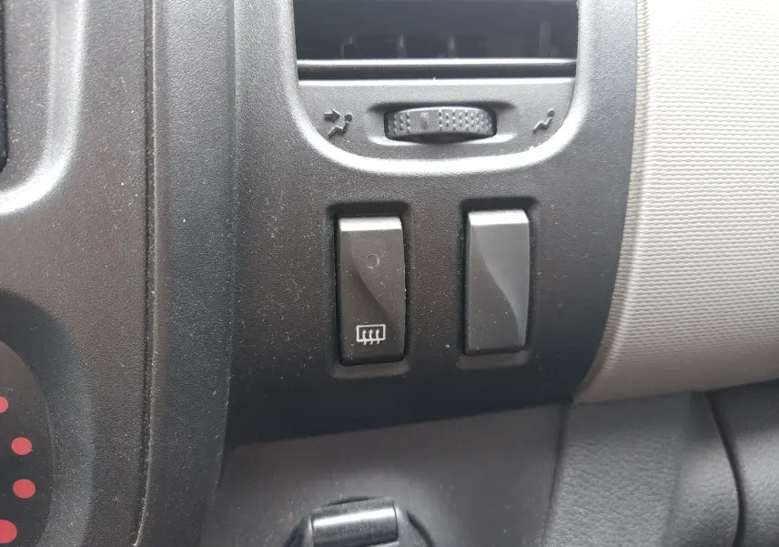 Gros plan sur les commandes de dégivrage et ventilation du tableau de bord noir du Renault Trafic Microbus blanc.