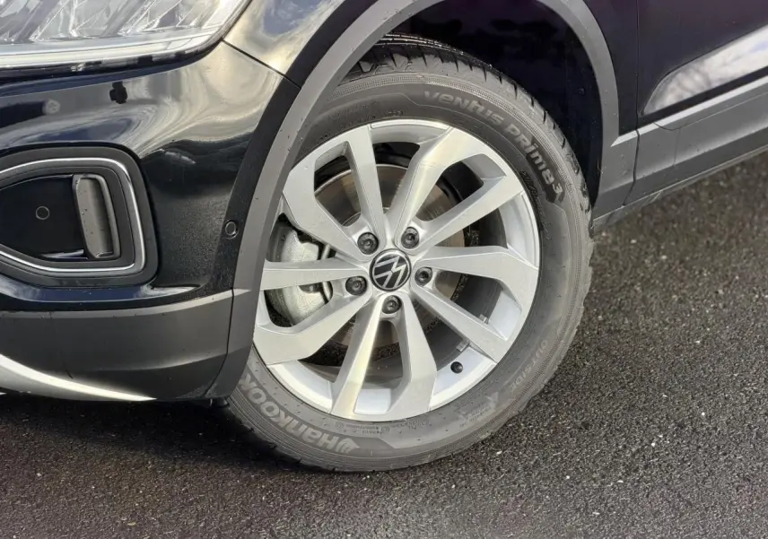 Gros plan sur la roue avant droite en alliage du Volkswagen T-Roc Deep Black avec partie avant du pare-chocs visible.