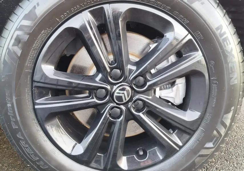 Gros plan sur la jante noire brillante d’une Citroën Berlingo 2025 avec logo central et pneu Nexen visible.