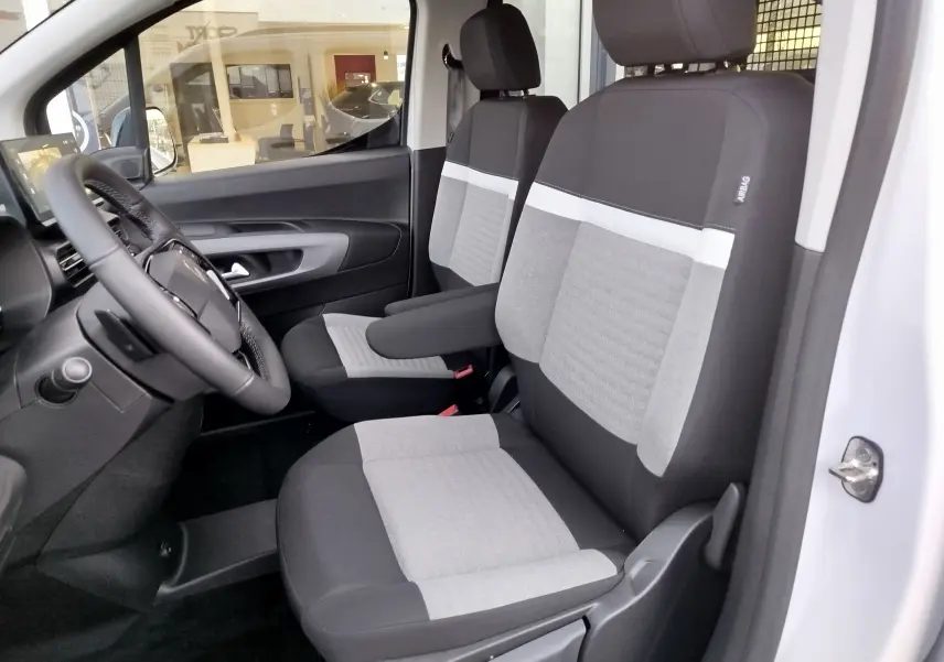 Vue intérieure côté conducteur du Citroën Berlingo 2025 blanc Kaolin, sièges tissu gris et noir avec accoudoir central.
