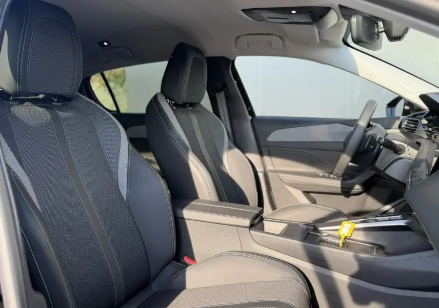 Intérieur de la Peugeot 308 2025 vu côté conducteur, sièges tissu et cuir gris avec accoudoir central.