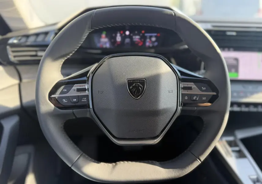 Vue rapprochée du volant cuir noir du Peugeot 308 2025 avec commandes intégrées et tableau de bord numérique flou.