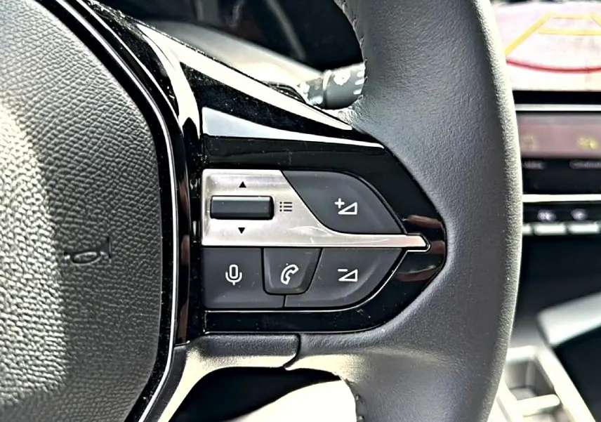 Gros plan sur le côté gauche du volant cuir noir d'une Peugeot 408 Hybrid 136 allure 2024 avec commandes vocales et téléphone.