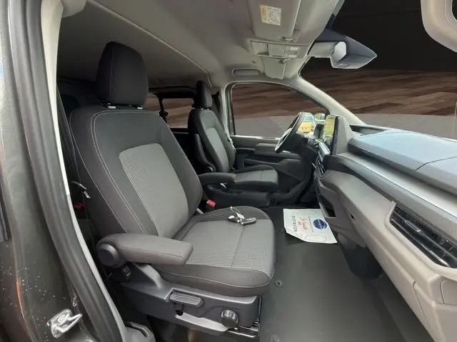 Vue intérieure côté conducteur du Volkswagen Transporter gris foncé 2026, montrant sièges tissu et tableau de bord moderne.
