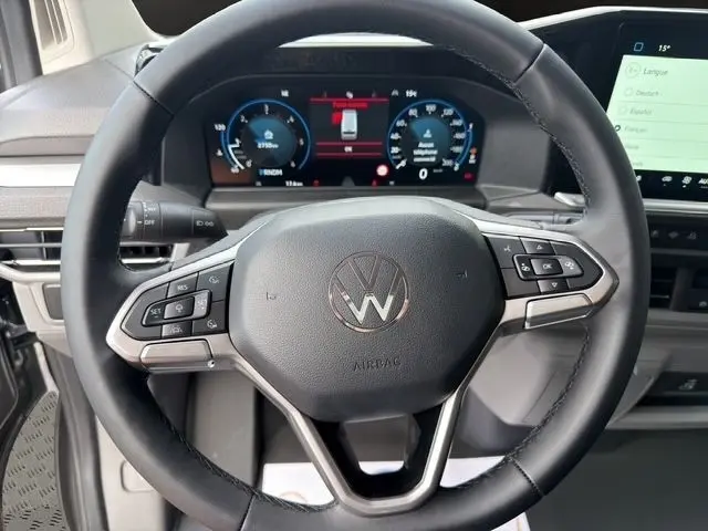 Vue rapprochée du volant multifonctions noir du Volkswagen Transporter gris foncé avec tableau de bord numérique en arrière-plan.