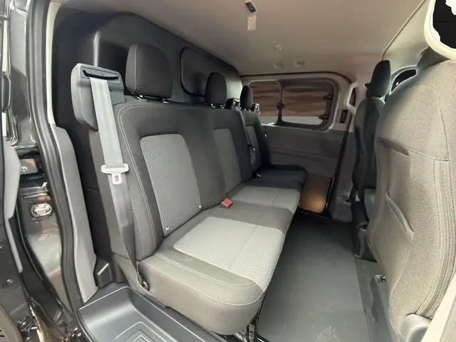 Vue intérieure côté droit du Volkswagen Transporter gris foncé, montrant la banquette arrière trois places et les sièges avant partiels.