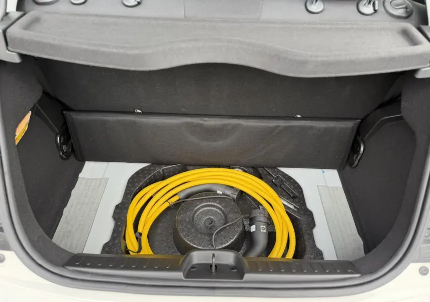 Coffre ouvert d'une Fiat 500 électrique blanc Artic, montrant le câble de recharge jaune rangé sous la tablette arrière.