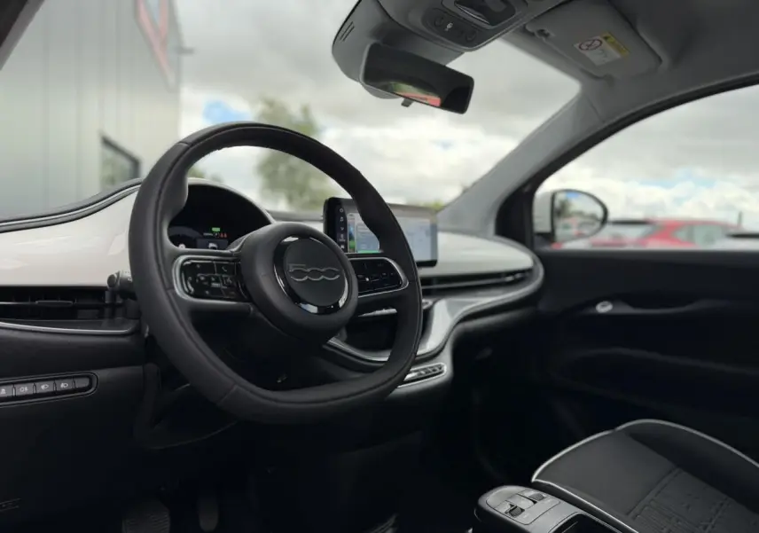 Vue intérieure côté conducteur du Fiat 500 électrique blanc Artic, avec volant noir Soft-Touch et écran tactile central.