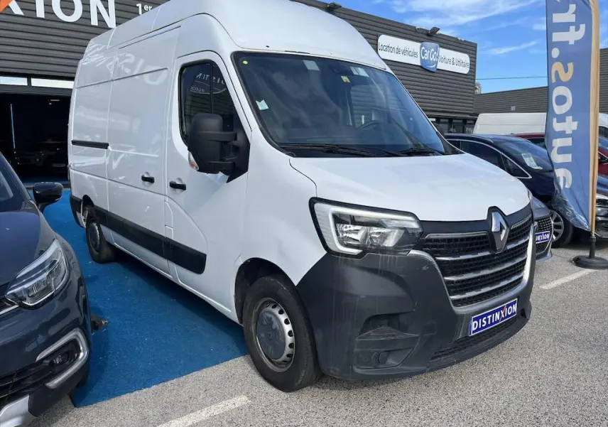 Vue 3/4 avant d’un utilitaire Renault Master blanc avec pare-chocs noir, stationné sur un parking extérieur.