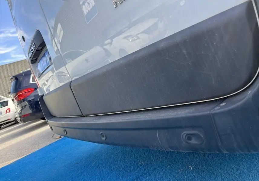 Gros plan sur le pare-chocs arrière noir d'un Renault Master blanc, avec logo et capteurs de recul visibles.