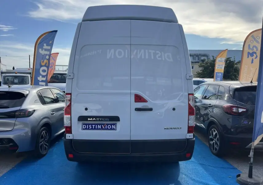 Vue arrière d'un utilitaire Renault Master blanc garé entre deux voitures, avec logo Distinxion visible sur la porte.