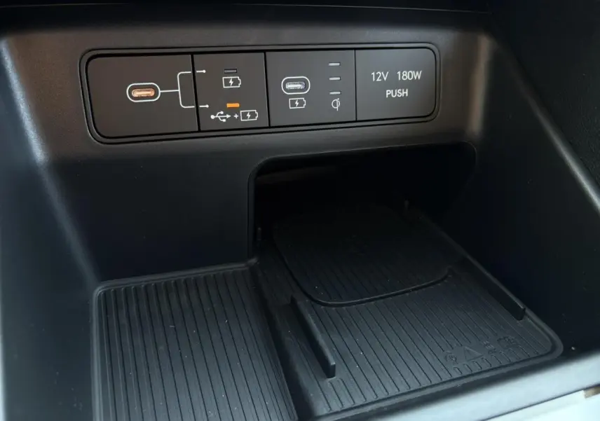 Gros plan sur la console centrale noire du Hyundai Tucson 2025 montrant prises USB, chargeur sans fil et prise 12V.