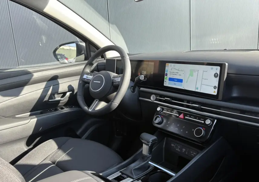 Intérieur avant gauche du Hyundai Tucson 2025 noir, tableau de bord moderne avec écran tactile panoramique et volant cuir.