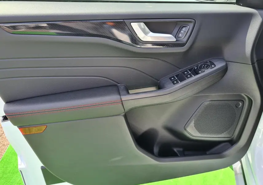 Gros plan sur la porte avant gauche du Ford Kuga blanc glacier, avec surpiqûres rouges et commandes électriques.