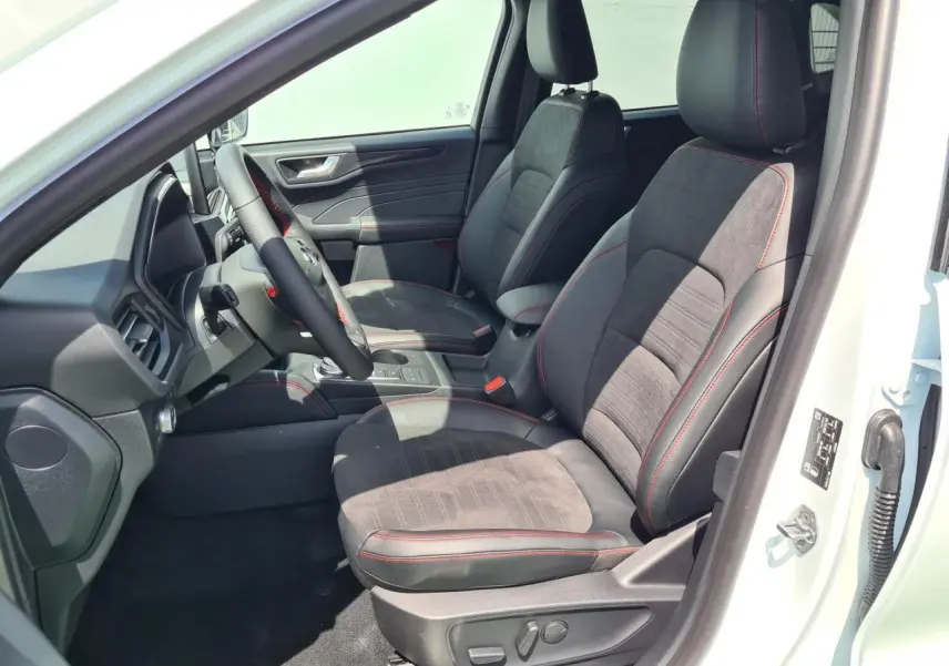 Vue intérieure côté conducteur du Ford Kuga blanc glacier 2022, sièges sport noirs avec surpiqûres rouges et volant ST-Line.